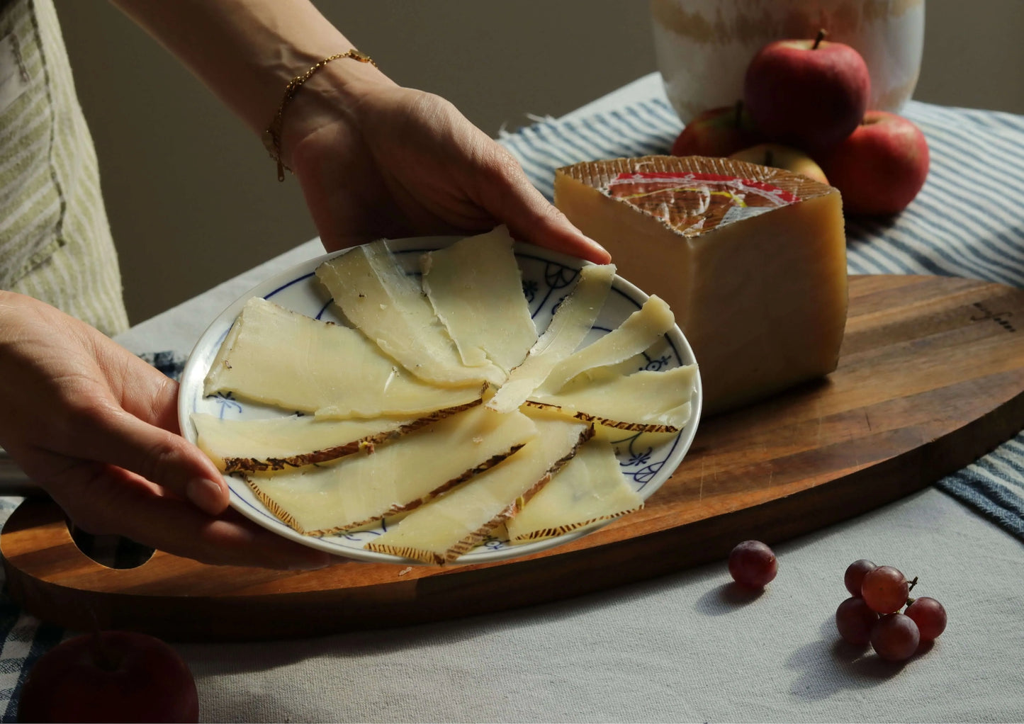 Gereifter Mischkäse (Queso de Mezcla Curado) in Scheiben auf einem Teller, daneben ein großes Käseviertel, dekoriert mit Äpfeln und Trauben.