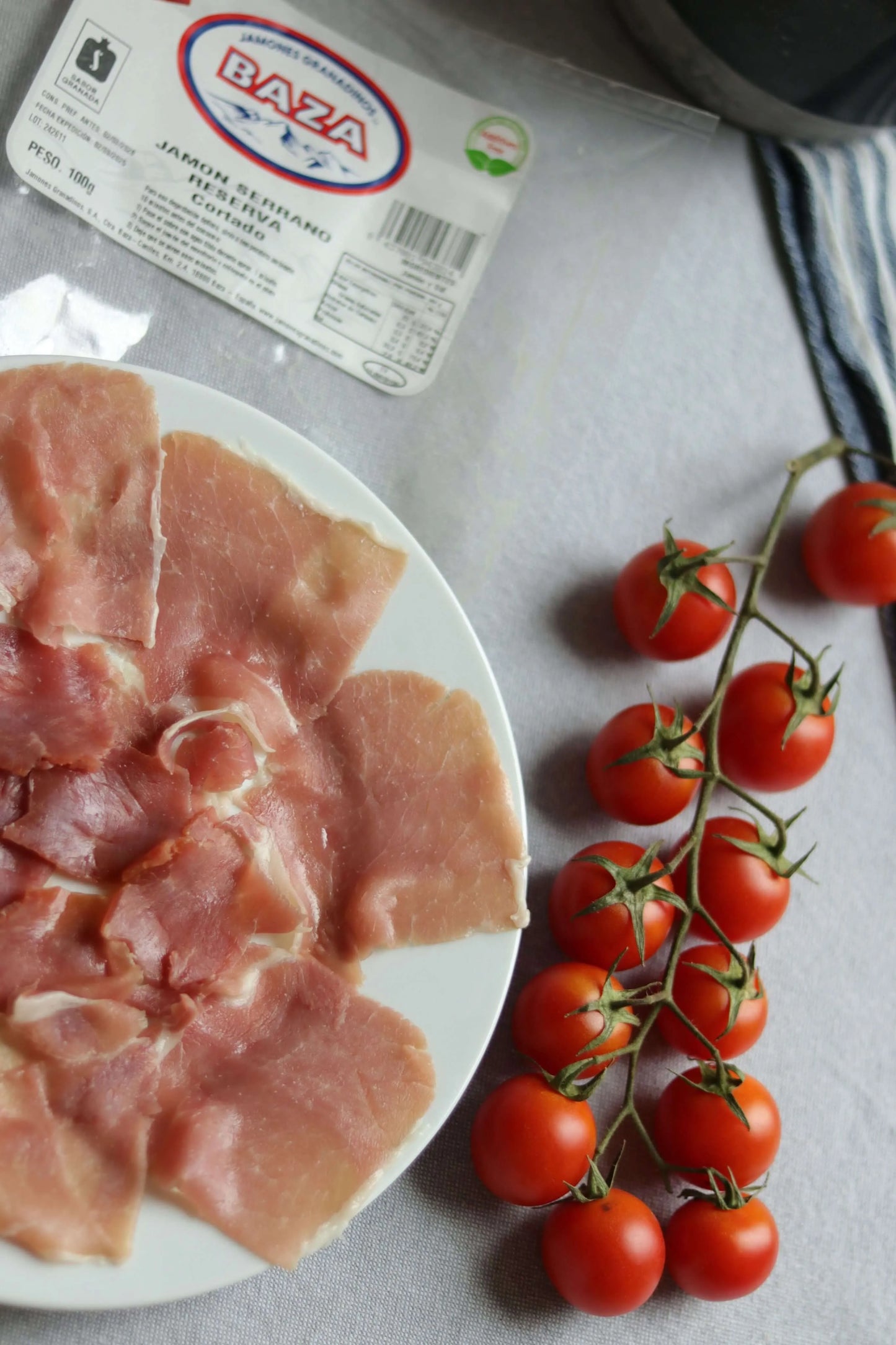 Teller mit dünn geschnittenem Serrano-Schinken Reserva (Jamón Serrano), dekoriert mit frischen Strauchtomaten.