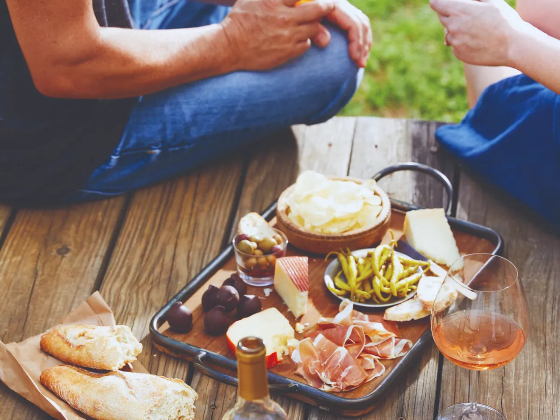 Mediterrane Tapasplatte mit Iberico Schinken, Käse, Oliven, Brot und Wein auf Holztisch im Freien.