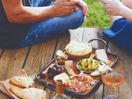 Mediterrane Tapasplatte mit Iberico Schinken, Käse, Oliven, Brot und Wein auf Holztisch im Freien.