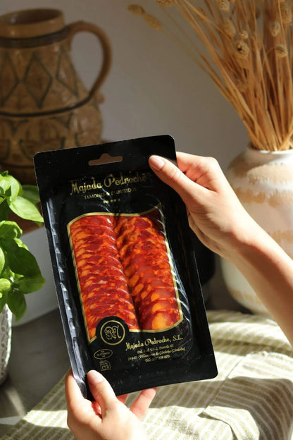 Aufschnittpackung Chorizo Ibérico de Bellota von Majada Pedroche, in der Hand gehalten, mit Kräutern und Keramik im Hintergrund.