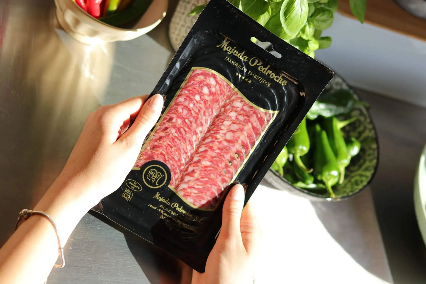 Aufschnittpackung Salchichón Ibérico de Bellota von Majada Pedroche, in der Hand gehalten, mit Gemüse im Hintergrund