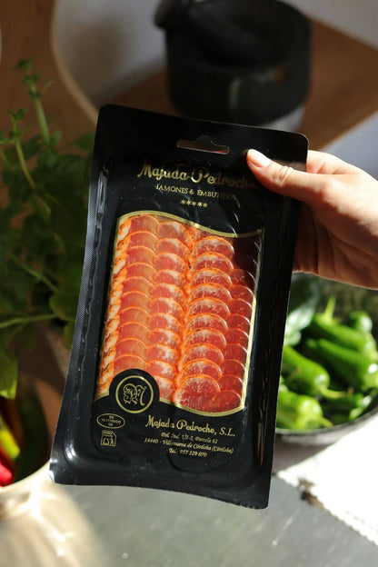Aufschnittpackung Schweinelende Ibérico de Bellota von Majada Pedroche, in der Hand gehalten, mit Gemüse im Hintergrund.