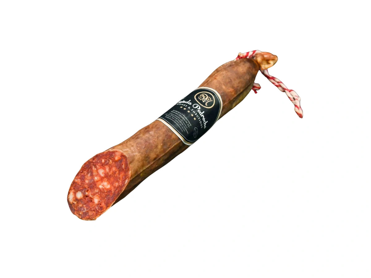 Ganze Stange Chorizo Ibérico de Bellota von Majada Pedroche, hergestellt aus Fleisch von iberischen Schweinen aus Eichelmast (Bellota), traditionell mit Pimentón de la Vera gewürzt und handwerklich gereift, vakuumverpackt für optimalen Frischeerhalt, freigestellt auf weißem Hintergrund.