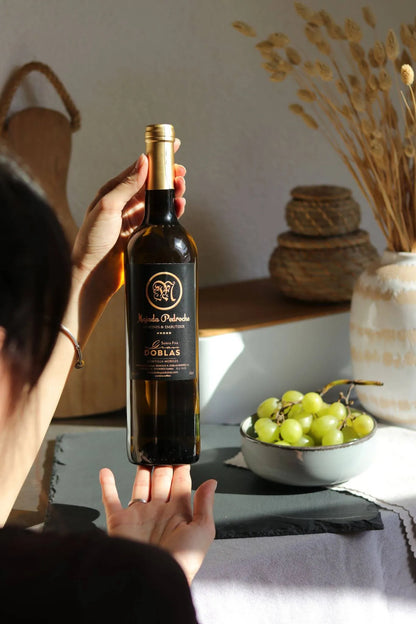 Flasche spanischer Weißwein von Majada Pedroche, in der Hand gehalten, im Hintergrund grüne Trauben und mediterrane Dekoration