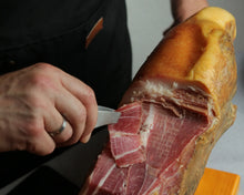 Gran Reserva Duroc Jamón am Knochen, mit einem Schinkenmesser frisch angeschnitten, mit ausgeprägter Marmorierung, intensiv roter Fleischfarbe und goldbrauner, luftgetrockneter Kruste.