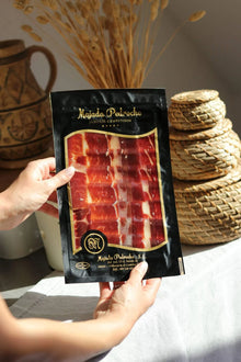 Hand hält Vakuumbeutel mit fein geschnittener Pata Negra Vorderschinken (Paleta) 100 % D.O.P. Los Pedroches, von Majada Pedroche, edle schwarze Verpackung mit Goldrand