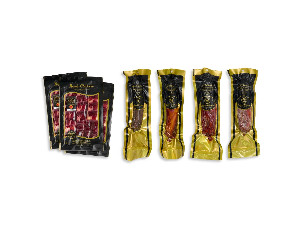Exklusive Genuss-Box von Majada Pedroche bestehend aus handgeschnittenem Jamón Ibérico de Bellota (2 x 100 g) in edlen schwarzen Blistern sowie vier verschiedenen ganzen Wurstspezialitäten (Lomo, Chorizo, Salchichón und Morcón), jeweils einzeln vakuumverpackt in Goldfolie, freigestellt auf weißem Hintergrund.