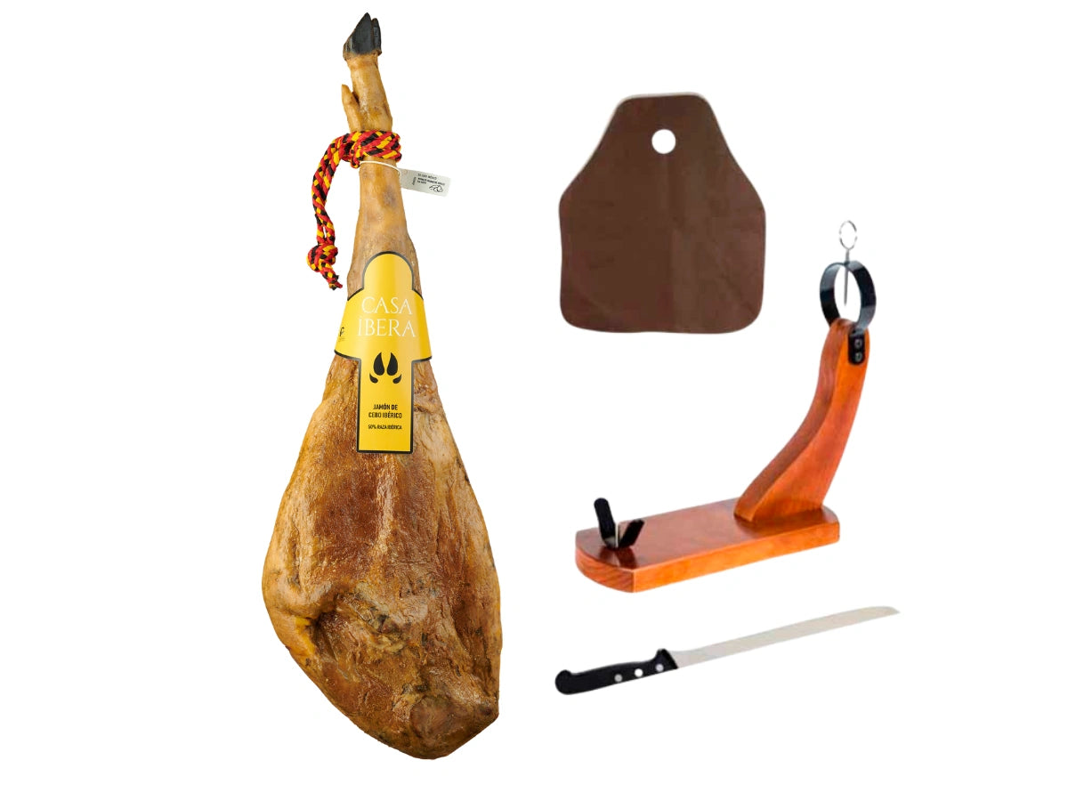Produktbild eines hochwertigen Iberico Schinken Sets auf weissem Hintergrund. Links ist ein ganzer Jamon Iberico de Cebo mit dunkler Klaue, rot-gelber Kordel und gelbem Casa Ibera Etikett dargestellt. Das Set beinhaltet rechts einen geschwungenen Schinkenhalter aus Holz mit schwarzem Metallring, ein langes, flexibles Schinkenmesser und eine dunkelbraune Abdeckung zum Schutz des Anschnitts.