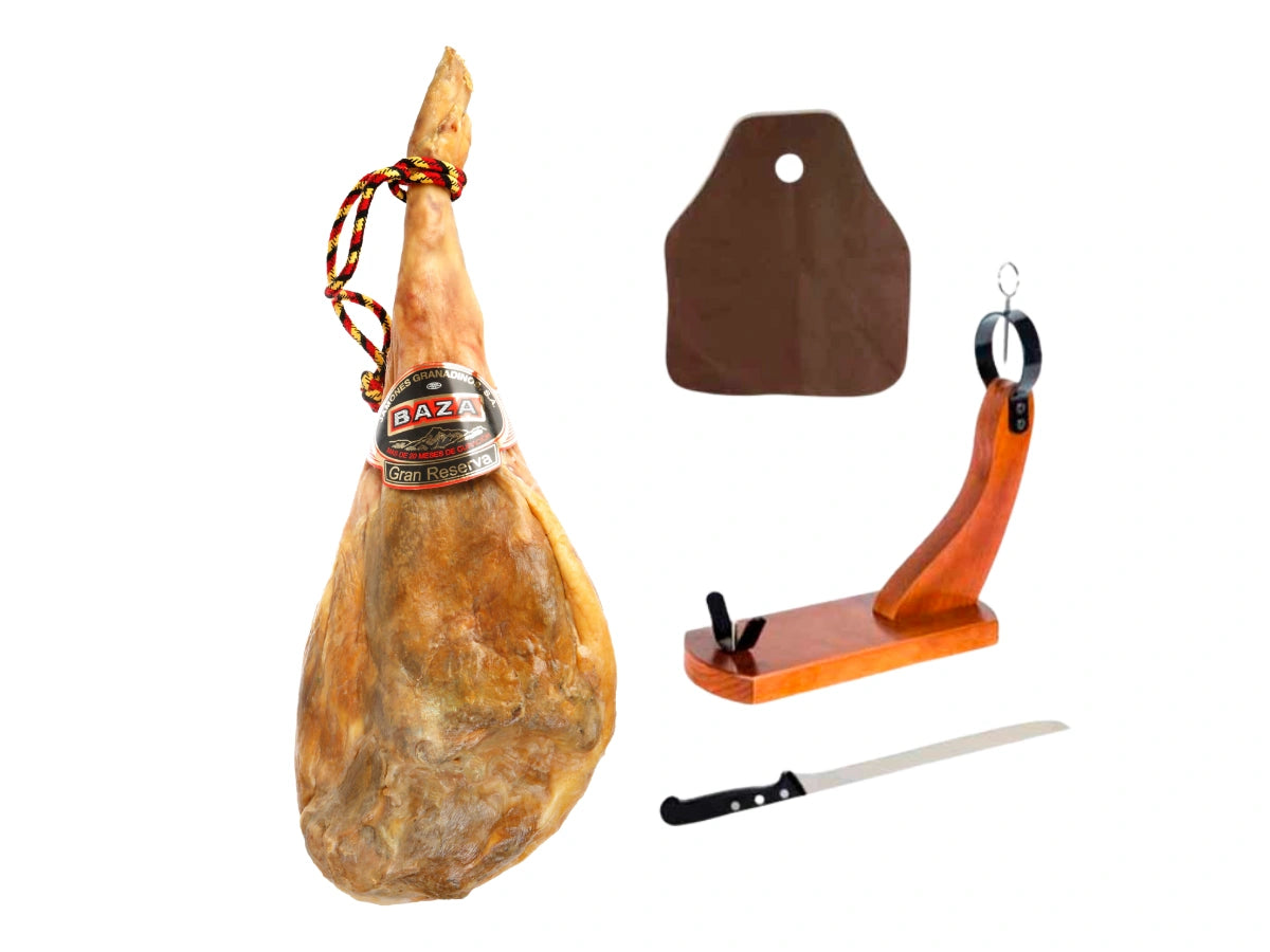 Produktbild eines kompletten Serrano Gran Reserva Schinken Sets vor weissem Hintergrund. Links steht ein ganzer, 24 Monate gereifter Gran Reserva Schinken mit rot-gelb-schwarzer Kordel und Baza Gran Reserva Etikett. Rechts daneben ist das Zubehoer abgebildet: ein Schinkenhalter aus Holz mit schwarzer Metallhalterung, ein langes Profi-Schinkenmesser mit schwarzem Griff und eine braune Schutzabdeckung fuer den Schinken.