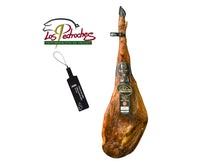 Produktbild eines exklusiven Jamon de Bellota 100 Prozent Iberico Pata Negra der Marke Majada Pedroche vor weissem Hintergrund. Der Premium-Schinken besitzt die geschützte Ursprungsbezeichnung Denominacion de Origen Los Pedroches, deren Logo oben links abgebildet ist. Das Stueck zeigt eine schlanke Form, eine schwarze Klaue und elegante dunkle Etiketten. Links ist die offizielle schwarze Plombe fuer reinen Iberico Eichelschinken zu sehen.