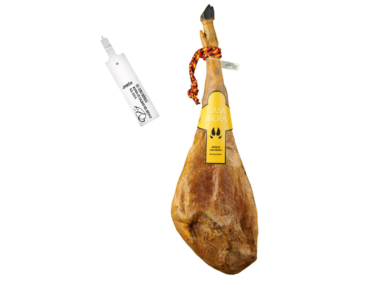 Produktbild eines ganzen Jamon de Cebo Iberico der Marke Casa Ibera auf weissem Grund. Der Schinken hat eine elegante, laengliche Form, eine dunkle Klaue und eine traditionelle rot-gelbe Kordel. In der Mitte befindet sich das markante gelbe Casa Ibera Etikett. Links wird die offizielle weisse Siegelplombe dargestellt, die die Echtheit und Einhaltung der Qualitaetsnorm fuer iberischen Cebo-Schinken bestaetigt.
