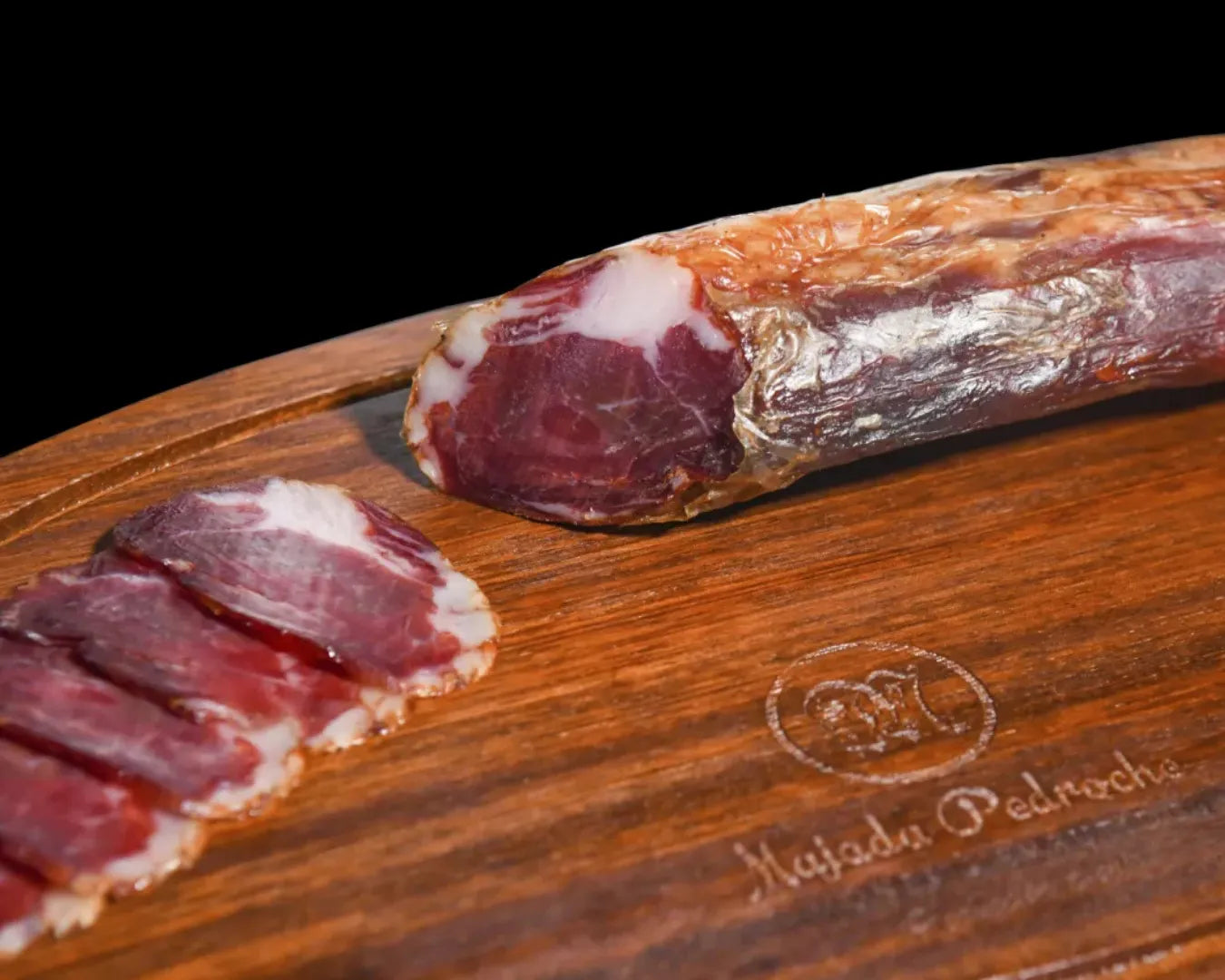 Ganzes Stück Lomito Ibérico de Bellota von Majada Pedroche auf einem Holzbrett, angeschnitten mit sichtbarer tiefdunkler Farbe und feiner weißer Fettmarmorierung der Presa Ibérica aus Los Pedroches