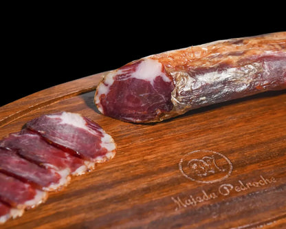 Ganzes Stück Lomito Ibérico de Bellota von Majada Pedroche auf einem Holzbrett, angeschnitten mit sichtbarer tiefdunkler Farbe und feiner weißer Fettmarmorierung der Presa Ibérica aus Los Pedroches