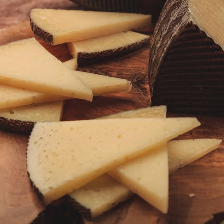 Geschnittener Manchego Käse auf Holzbrett mit rustikaler Rinde typisch spanischer Schafskäse
