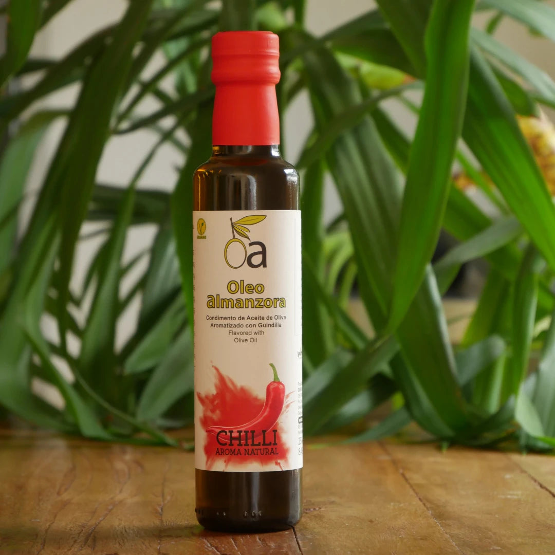 Flasche aromatisiertes Olivenoel mit Chili auf Holztisch vor gruenem Pflanzenhintergrund