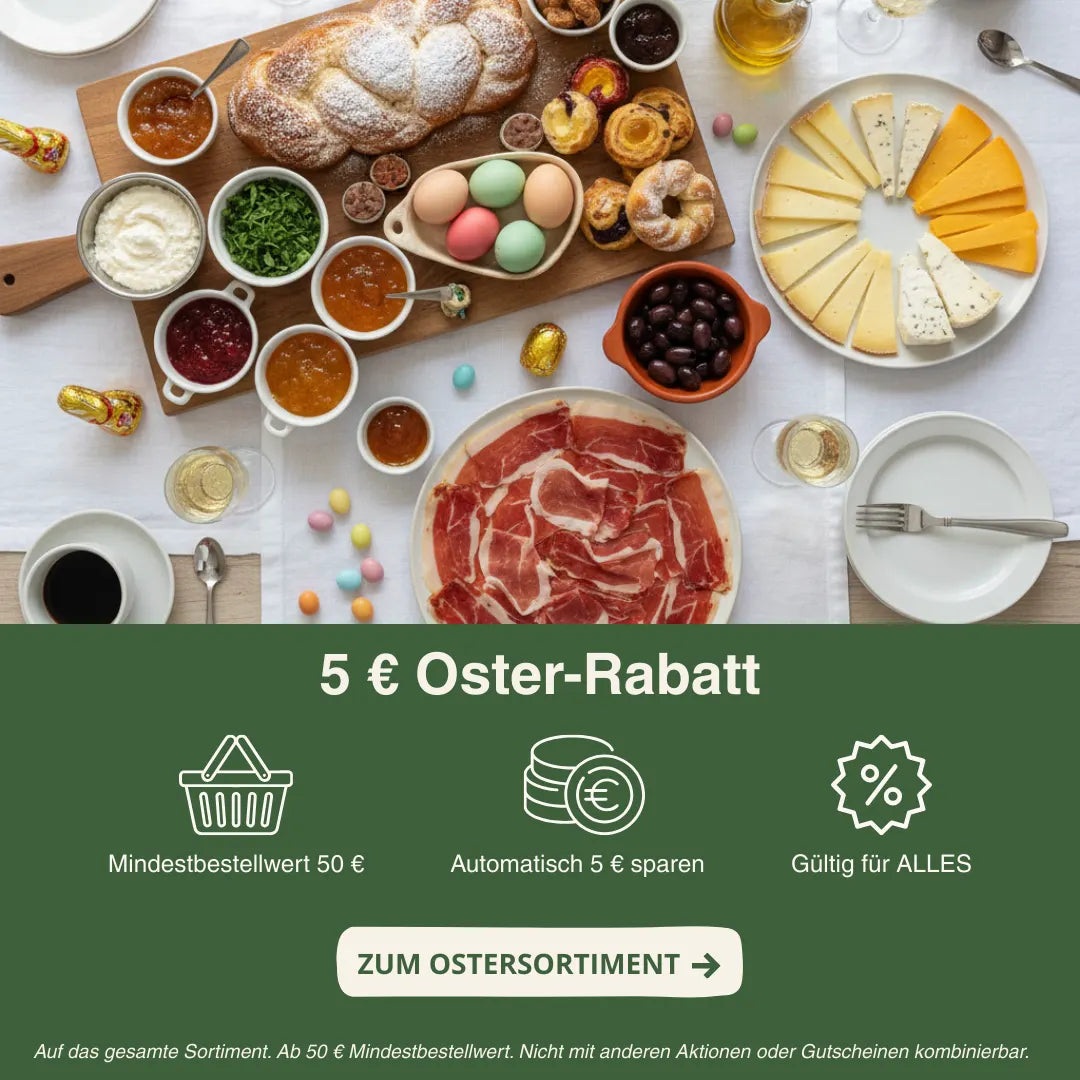 Großes Osterfrühstück mit Serrano-Schinken, Käseauswahl, Brot, Oliven, Marmeladen und bunten Ostereiern. Hinweis auf 5 € Oster-Rabatt ab 50 € Mindestbestellwert.