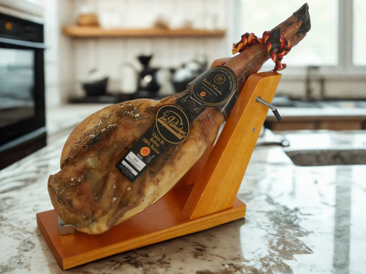 Ganze Paleta Pata Negra 100 % Ibérica von Los Pedroches auf einem Holz-Schinkenhalter in einer Küche.