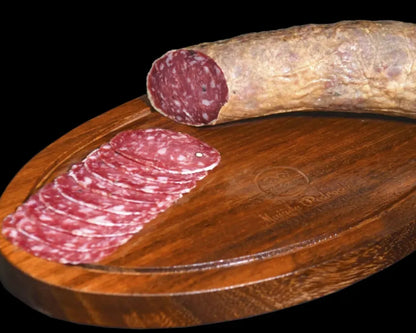 Halbes Stück Salchichón Ibérico de Bellota von Majada Pedroche auf einem Holzbrett, daneben aufgefächerte dünne Scheiben mit sichtbarer Pfefferkörnung und typischer Bellota-Marmorierung