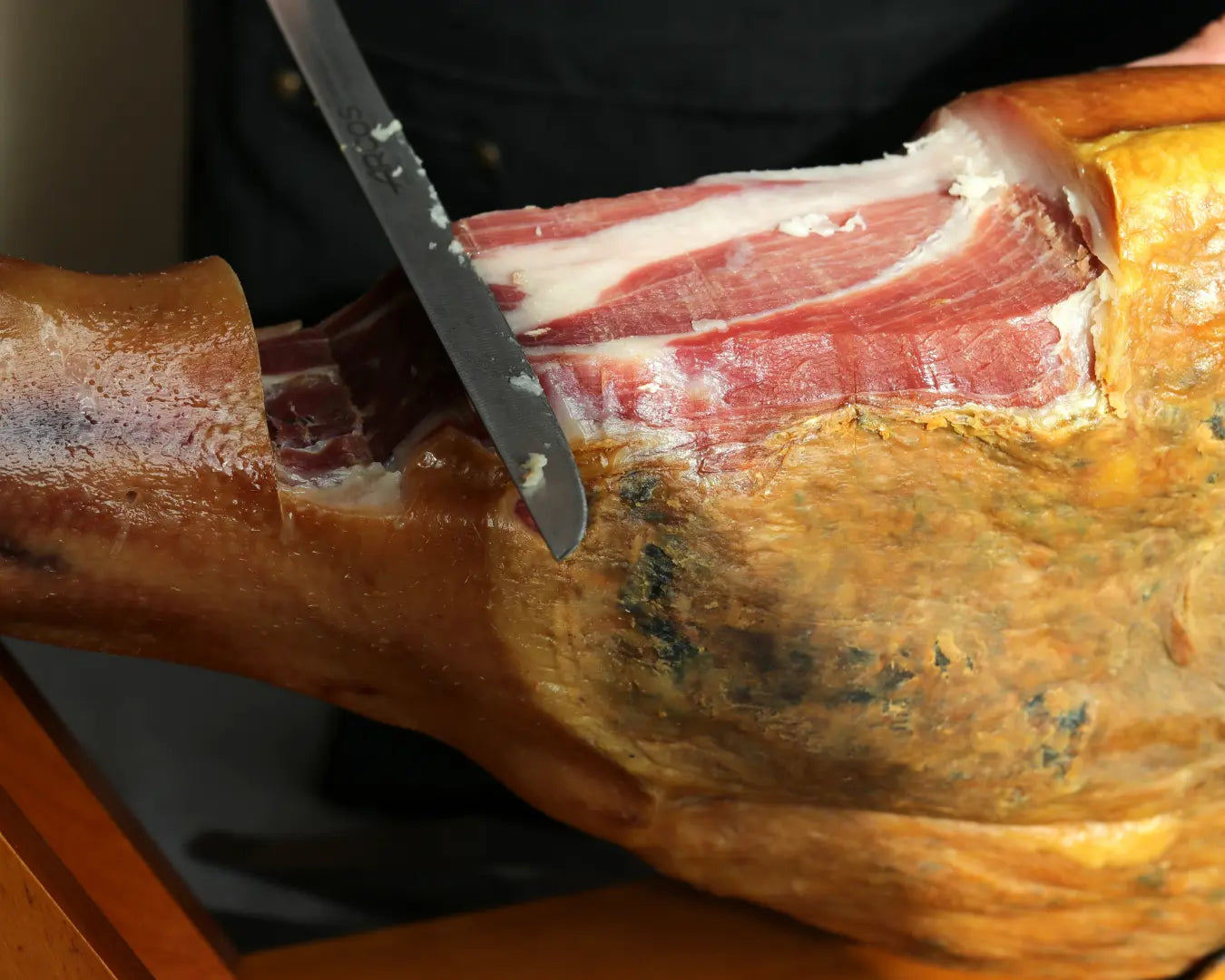 Serrano Reserva Jamón am Knochen, frisch mit einem langen Schinkenmesser angeschnitten, sichtbare Marmorierung und gereifte Kruste des luftgetrockneten spanischen Schinkens.