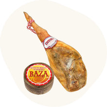 Set mit einem ganzen Reserva Schinken von Baza und einem runden, gereiften Mischkäse, beide mit sichtbarem Etikett.