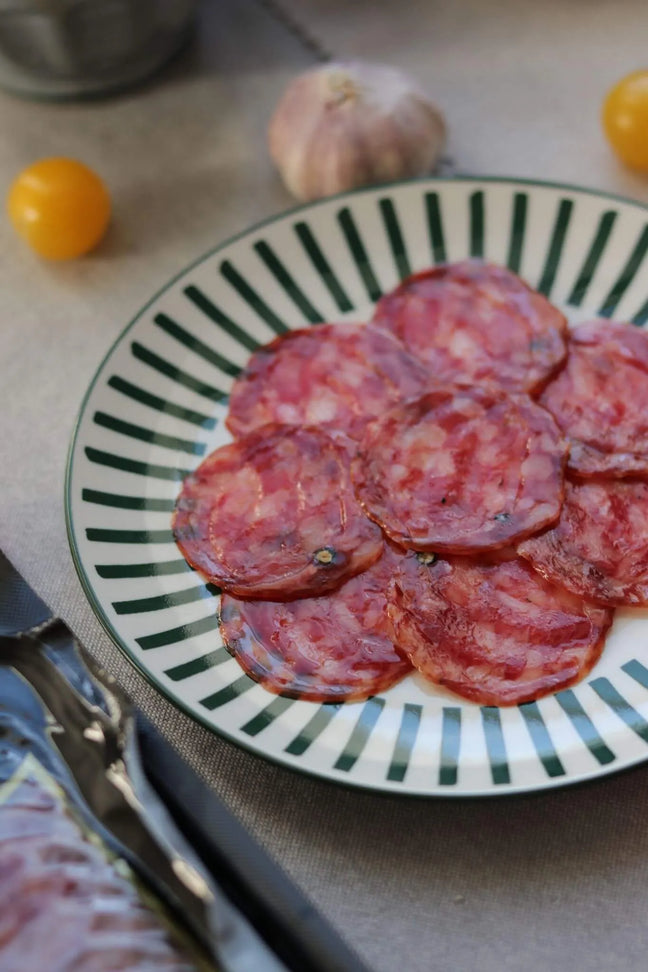 Spanischer Salchichón Aufschnitt auf Teller mit Knoblauch und Tomaten