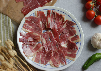 Teller mit dünn geschnittenem Jamón Serrano Gran Reserva (Schinken) auf weiß-blauem Teller, dekoriert mit Knoblauch und grüner Paprika