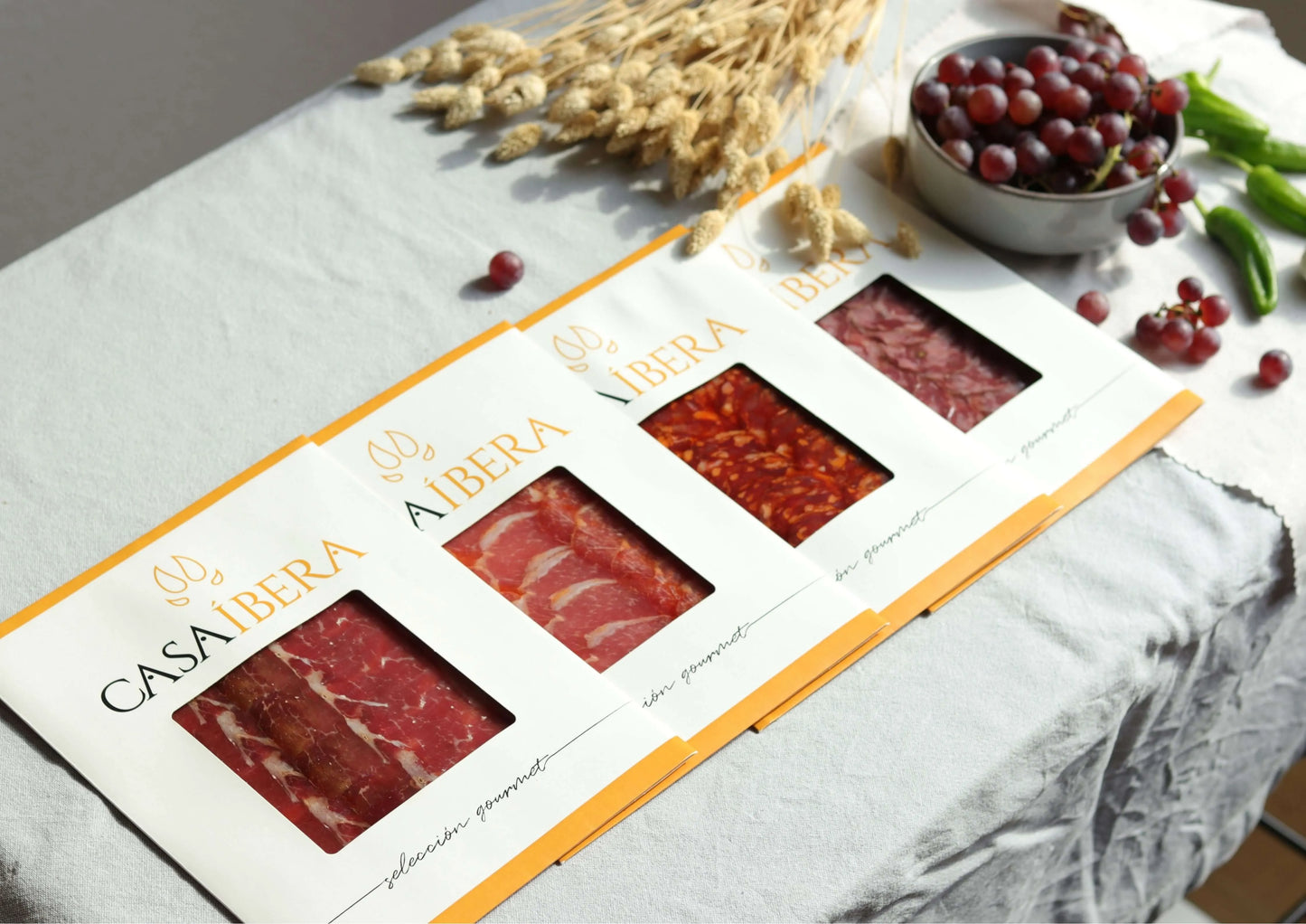 Vier Packungen „Casa Íbera“ mit iberischem Aufschnitt nebeneinander auf einem Tisch. Sichtbar sind Schweinelende (Lomo), Jamón Ibérico (Schinken), Chorizo und Salami (Salchichón)