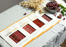 Vier Packungen „Casa Íbera“ mit iberischem Aufschnitt nebeneinander auf einem Tisch. Sichtbar sind Schweinelende (Lomo), Jamón Ibérico (Schinken), Chorizo und Salami (Salchichón)