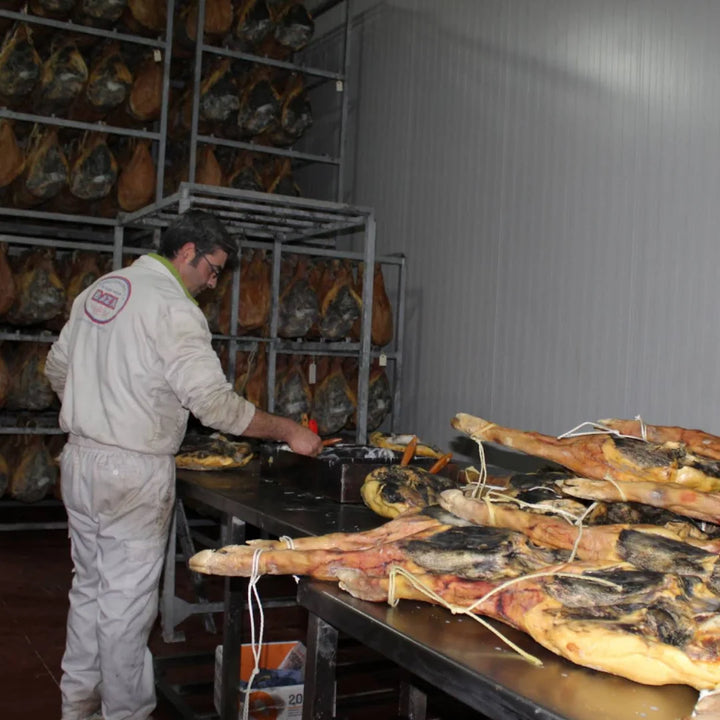 Mitarbeiter von Jamones Granadinos Baza bei der handwerklichen Verarbeitung von Serrano-Schinken im Reifekeller – traditionelle Herstellung in Granada, Andalusien