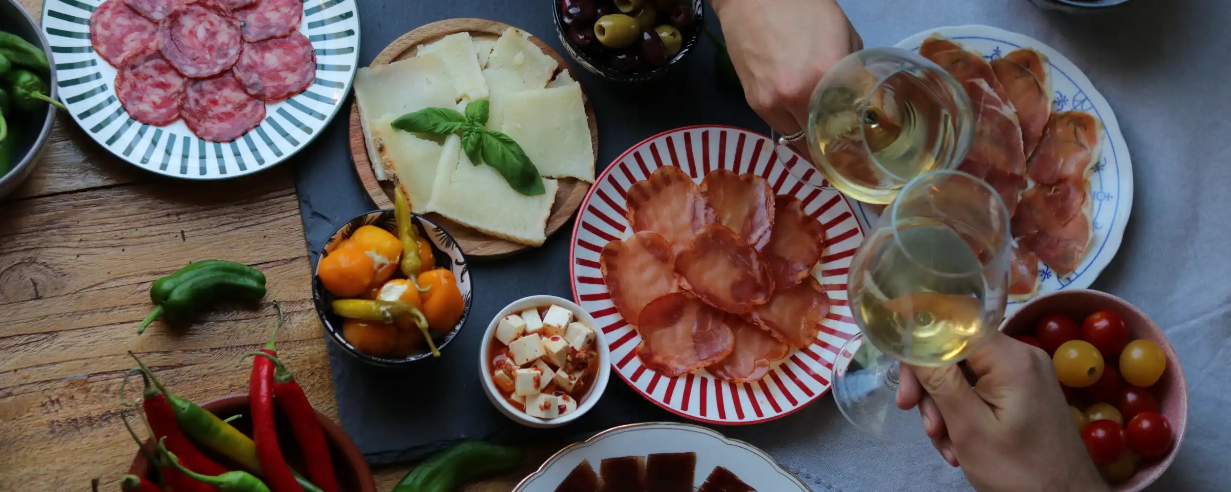 Spanische Tapas-Tafel von oben mit Jamón, Käse, Lomo, Oliven, Paprika und Weißwein – Lifestyle-Banner für spanische Firmengeschenke von La Tradición