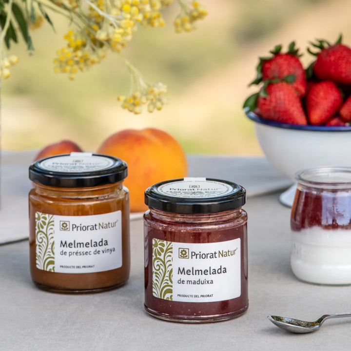 Zwei Gläser Mermelada von Priorat Natur – Pfirsich und Erdbeere – auf grauem Untergrund mit frischen Früchten und Blumen, Produkte aus dem Priorat, Katalonien